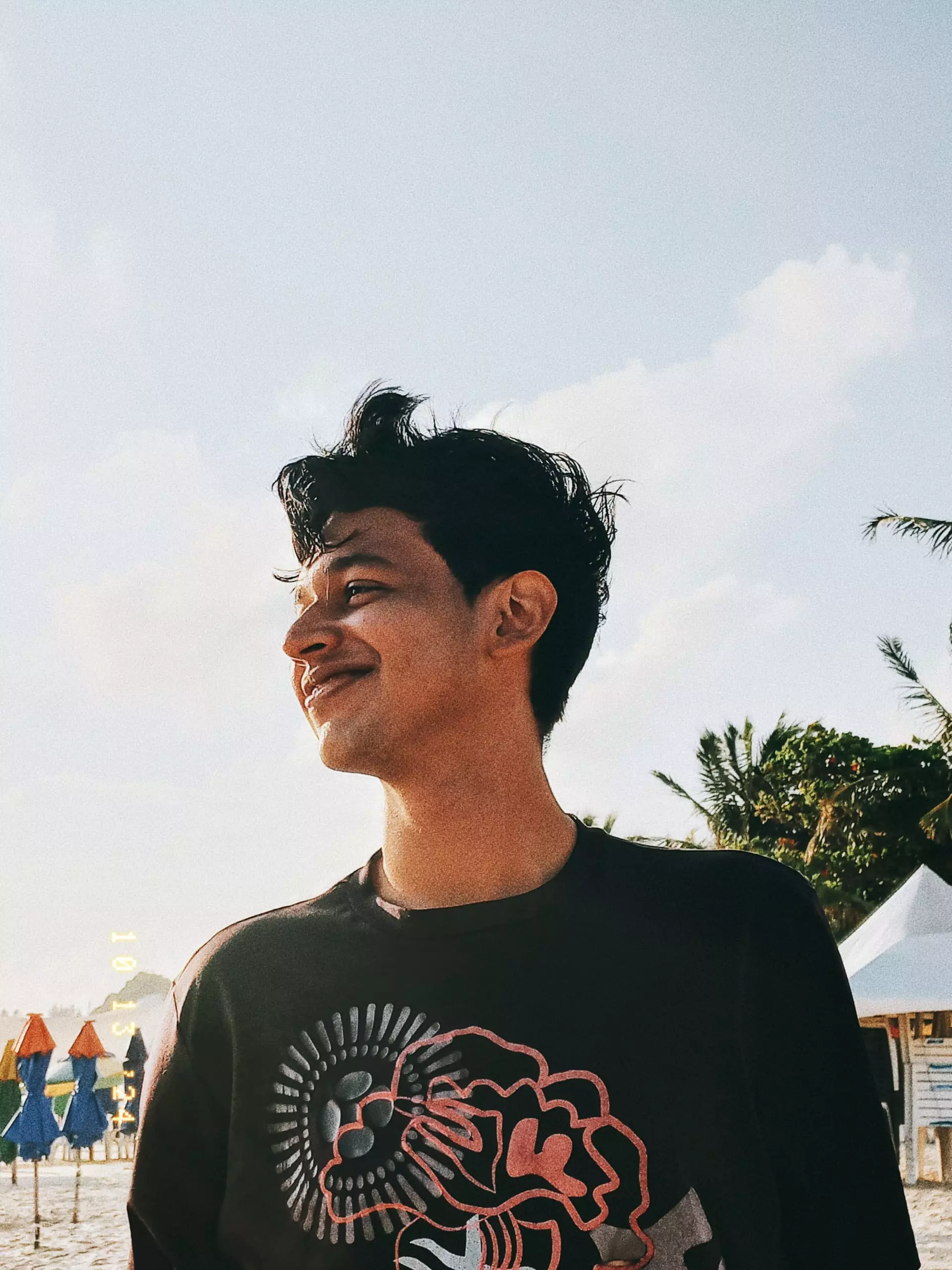 Kauan Leandro sorrindo, olhando para o lado ao ar livre durante o dia, com árvores ao fundo.