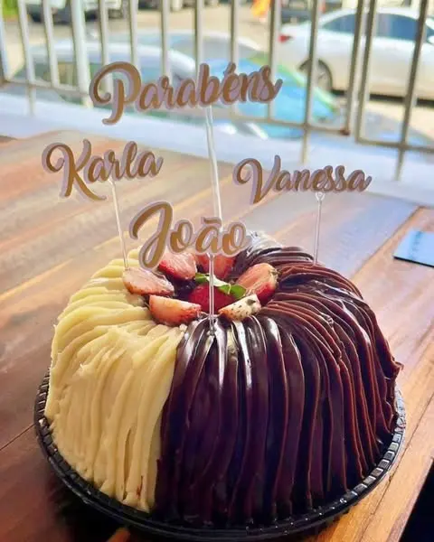 Bolo com cobertura de chocolate e baunilha, decorado com frutas vermelhas e mensagem para Karla, Vanessa e João